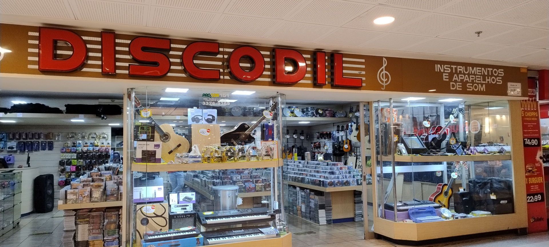 Fachada da liloja "Discodil - instrumentos e aparelhos de som" é possível ver uma vitrine envidraçada com diversos instrumentos musicais. Dentro e possível ver bancadas com CDs e DVDs